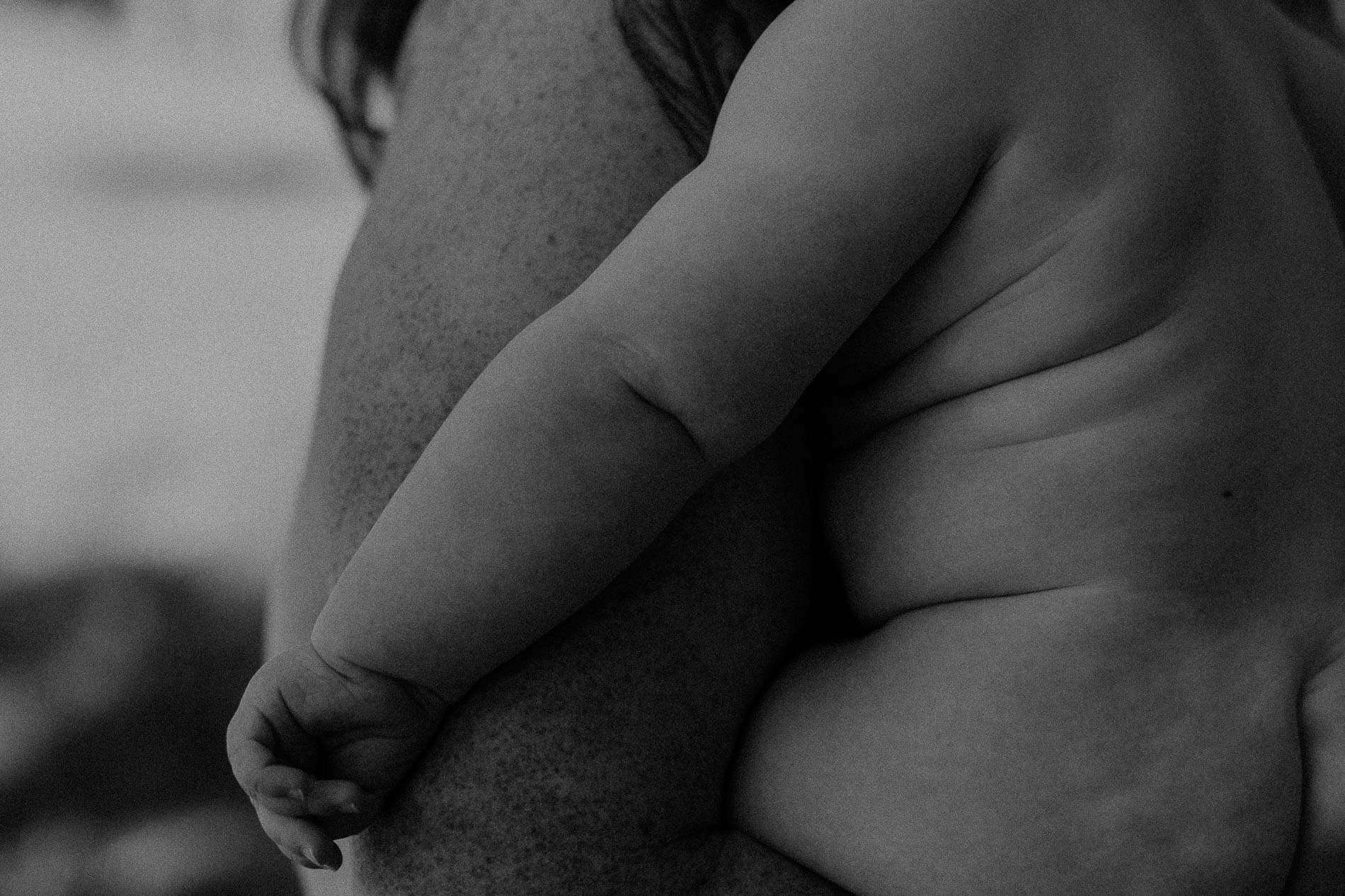 Nærbilde av en baby som holder rundt sin mors arm, svart-hvitt.