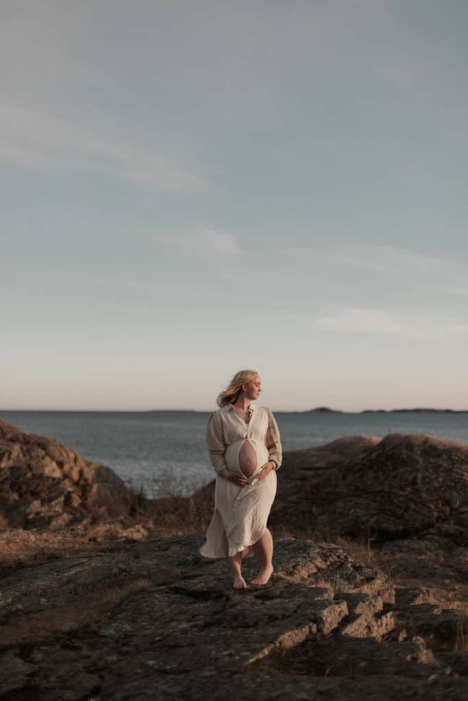 Kvinne i hvit kjole holder ballong ved sjøen på en rolig dag.