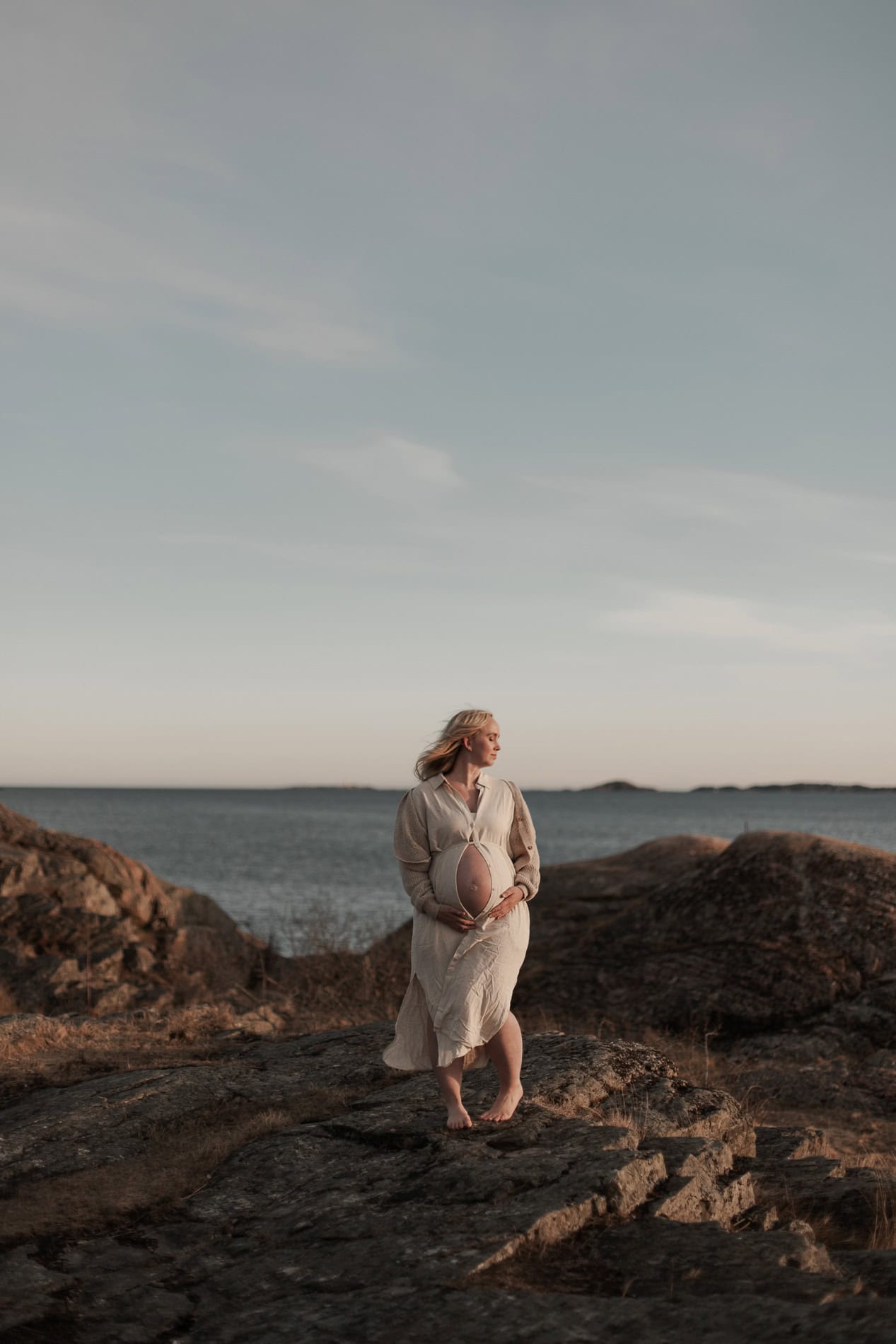 Kvinne i hvit kjole holder ballong ved sjøen på en rolig dag.
