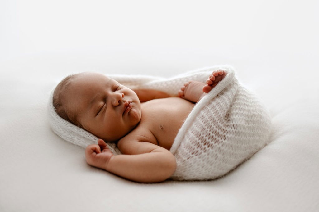 Nyfødt baby sovende, portrett av en liten baby innpakket i hvitt teppe.