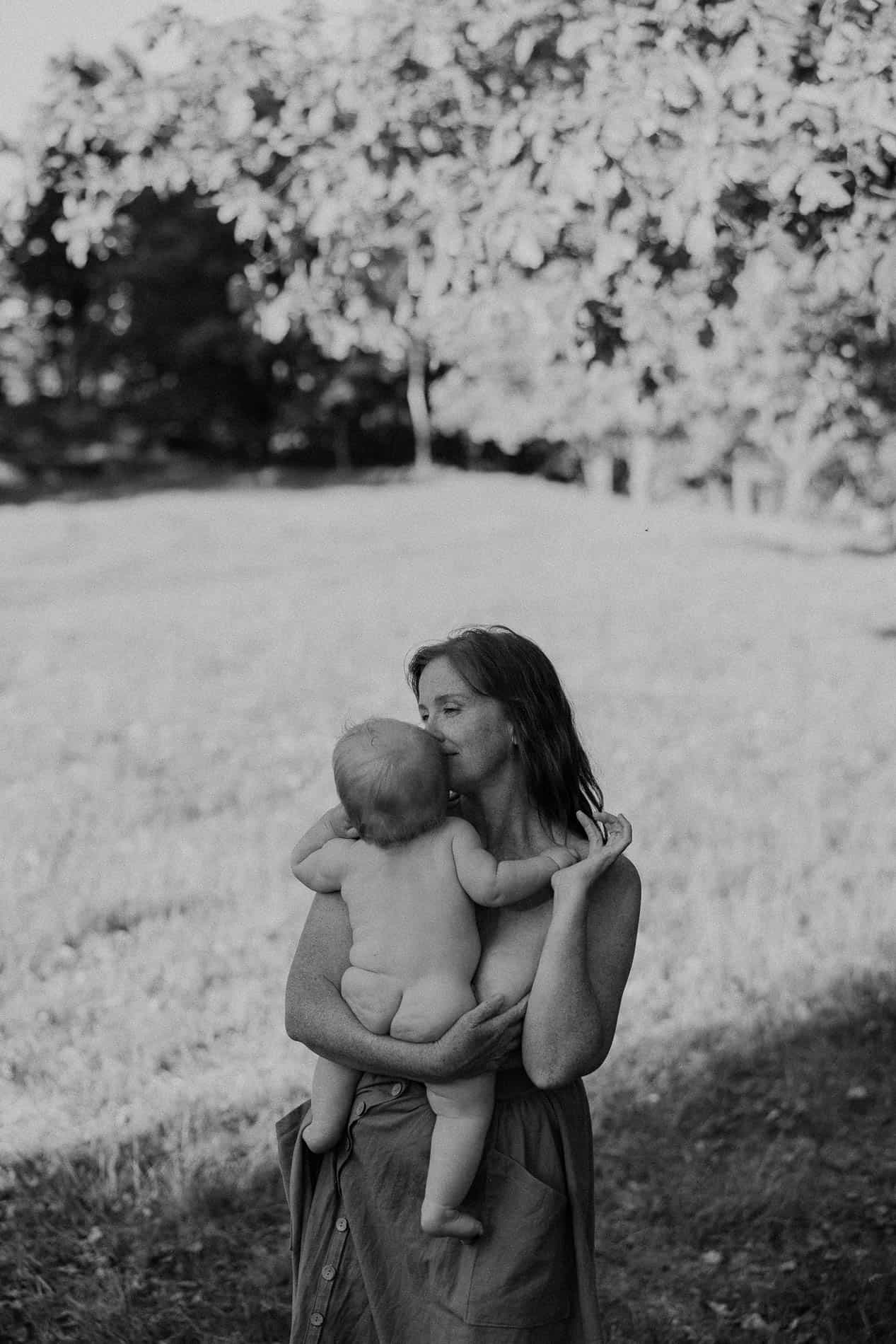 Mor holder baby i armene i utendørs miljø, svart-hvitt bilde.